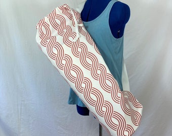 May include: A white yoga mat bag with a red and white wavy pattern. The bag has a drawstring closure and a long strap.