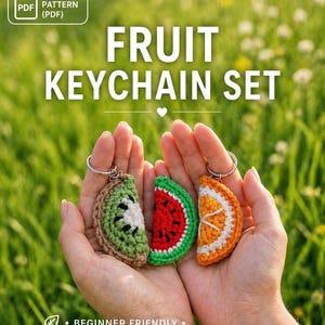 May include: Three crocheted fruit keyrings: a kiwi, watermelon, and orange slice. The keyrings are held in open hands against a blurred green background. Text reads "FRUIT KEYCHAIN SET" and "BEGINNER FRIENDLY".