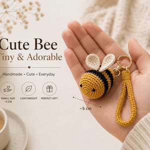 May include: A crocheted bee keychain with yellow and black stripes, white wings, and a yellow wrist strap attached to a gold metal ring. The text on the image reads Cute Bee Tiny & Adorable, Handmade, Cute, Everyday, Small Size ~5 cm, Lightweight, Perfect Gift.