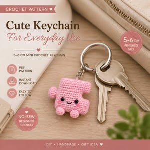 Puede incluir: Un llavero de ganchillo rosa con forma de pieza de rompecabezas, con cara sonriente, ojos negros y mejillas rosadas. El llavero está unido a una anilla de metal plateado con dos llaves. El texto dice Crochet Pattern, Cute Keychain For Everyday Use, 5-6 cm Mini Crochet Keychain, PDF Pattern, Instant Download, Easy To Follow, No-Sew Beginner Friendly, DIY, Handmade, Gift Idea.