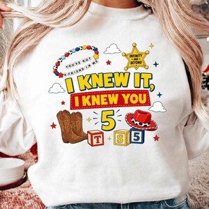 Pu&ograve; includere: Una felpa bianca con una stampa grafica che riporta il testo I KNEW IT, I KNEW YOU, un braccialetto di perline con il testo YOU'VE GOT A FRIEND IN ME, una stella da sceriffo gialla, stivali da cowboy marroni, un cappello rosso e blocchi con T, S, 5.