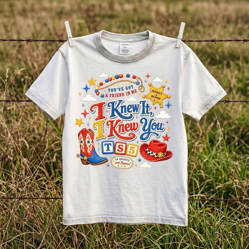 Puede incluir: Una camiseta gris claro de manga corta con un estampado gr&aacute;fico colorido que incluye una bota de vaquero, un sombrero rojo, una estrella de sheriff y el texto: You've Got A Friend In Me, I Knew It, I Knew You, TS5 y To Infinity And Beyond.