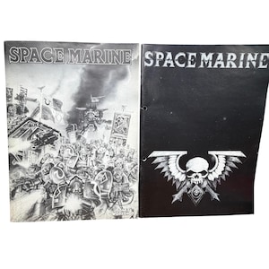 May include: Two Space Marine game manuals. The left manual features a black and white battle scene with soldiers and a large mechanical walker. The right manual has a black cover with the text Space Marine and a white winged skull emblem.