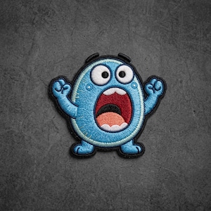 May include: An embroidered patch featuring a round, light blue creature with a surprised expression, wide white eyes, and a large open mouth showing a dark red interior, a black throat, and a light peach-colored tongue, all outlined in black thread.