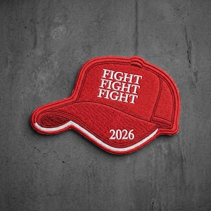 May include: A red embroidered patch shaped like a baseball cap with white stitching. The text FIGHT FIGHT FIGHT is embroidered in white on the front panel, and the number 2026 is embroidered in white along the curved brim of the cap.