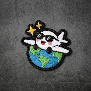 May include: An embroidered patch featuring a white cartoon airplane wearing black sunglasses, positioned above a blue and green globe. The design includes two yellow four-pointed stars and is outlined with a thick black border on a dark background.