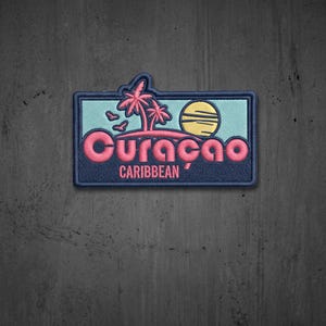 May include: A rectangular embroidered patch featuring a light blue background with a pink palm tree graphic, a yellow sun, and the text Curaçao in pink letters above the word CARIBBEAN in smaller pink letters, all bordered by a dark blue frame.