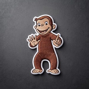 May include: An embroidered patch featuring a brown monkey with a light tan face, hands, and feet. The monkey is smiling with its mouth open, showing teeth, and is holding up one hand with five fingers extended and the other hand with one finger up.