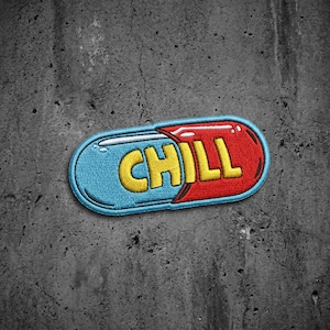 May include: An embroidered patch shaped like a capsule pill, featuring a light blue left side and a red right side. The word CHILL is stitched in bold yellow capital letters across the center of the pill, outlined with a thick blue border.