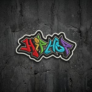 May include: An embroidered patch featuring the word HIPHOP in a stylized graffiti font. The letters are colored in red, yellow, green, blue, and purple with a thick black outline and a white border, creating a bold, multi-colored design.