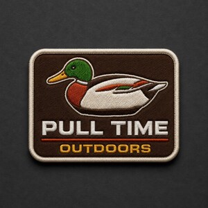 May include: A rectangular embroidered patch with a dark brown background featuring a mallard duck with a green head, yellow bill, and white body. The text PULL TIME is in white, and OUTDOORS is in yellow, separated by a thin horizontal orange line.