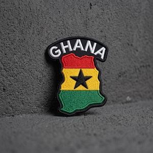May include: An embroidered patch shaped like the map of Ghana featuring horizontal red, yellow, and green stripes with a centered black star. The word GHANA is stitched in white capital letters on a black arched border at the top of the patch.