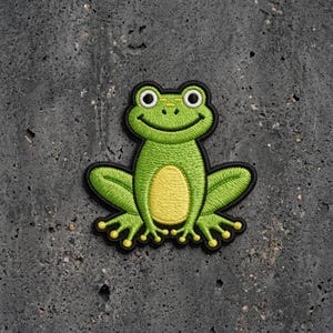 May include: An embroidered patch featuring a bright green frog with a pale yellow belly, large white eyes with black pupils, and a wide smiling mouth. The frog is depicted in a seated position with splayed legs and webbed feet, outlined in black.
