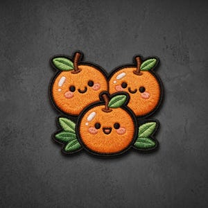May include: An embroidered patch featuring three bright orange citrus fruits with smiling faces, rosy cheeks, and small green leaves. Each orange has a black stitched border, white highlights, and a textured thread finish on a dark background.