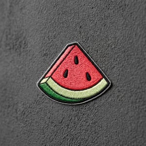 May include: A triangular watermelon slice patch featuring embroidered red fruit flesh with three black seeds, a thin white rind, and a green outer edge. The design is finished with a dark grey border, showcasing detailed thread work throughout the piece.