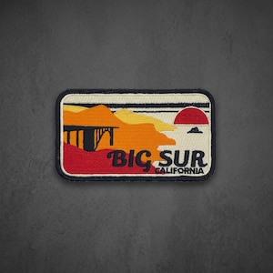 May include: A rectangular embroidered patch featuring a landscape of Big Sur, California. The design includes orange and yellow mountains, a black bridge silhouette, a red sun, and the text BIG SUR CALIFORNIA in black against a cream background.