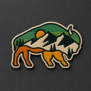 May include: An embroidered patch shaped like a bison, featuring a landscape design with green hills, dark green mountains, a yellow sun, and orange and yellow legs. The entire patch is outlined with a thick, cream-colored stitched border.