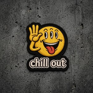 May include: An embroidered patch featuring a yellow circular face with three eyes, a wide grinning mouth with a red tongue sticking out, and a hand raised in a wave. Below the face, the text chill out is stitched in white with a black outline.