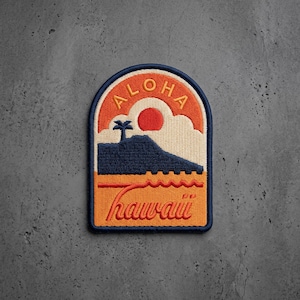 May include: An embroidered patch with an arched top featuring a dark blue mountain silhouette, a small palm tree, and a red sun against a cream sky. The word ALOHA is arched at the top in orange, and the word hawaii is written in orange script below.