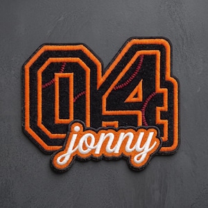 May include: A black and orange embroidered patch featuring the number 04 with baseball-style red stitching details. The name jonny is embroidered in white cursive script across the bottom of the numbers, outlined in orange and black thread.