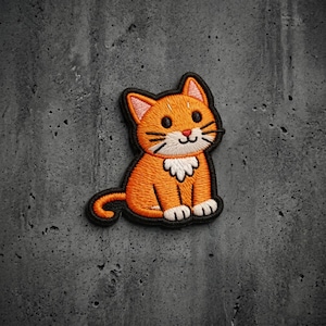 May include: An embroidered patch featuring a cartoon orange tabby cat with a white chest patch, white paws, and black whiskers. The cat has large black eyes, a small pink nose, and a curved tail, all outlined in a thick black border.
