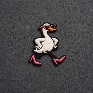 May include: An embroidered patch featuring a white goose with an orange beak, wearing pink sunglasses and pink high-heeled shoes. The goose is depicted in a walking pose with its wings on its hips, outlined in black thread against a dark background.