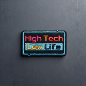 May include: A rectangular embroidered patch with a black background and a bright blue border. The text High Tech is stitched in red and orange, while the text Low Life is stitched in yellow and black, set against a light blue rectangular bar.
