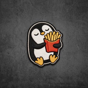May include: An embroidered patch featuring a black and white penguin with closed eyes, holding a red carton filled with golden yellow french fries. The design has a thick black border and is rendered in a textured, stitched style with vibrant colors.