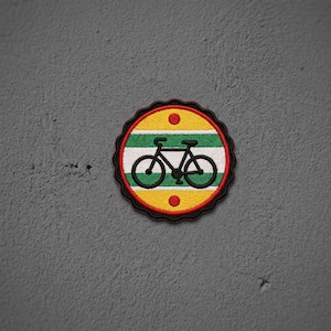 May include: A circular embroidered patch with a scalloped black border. The design features horizontal stripes of yellow, green, and white, with a black bicycle silhouette in the center and a small red dot above and below the bicycle.