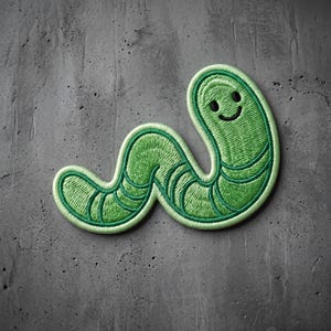 May include: An embroidered patch shaped like a green worm with a smiling face. The design features a light green border, darker green segmented body lines, and two small black circular eyes with a curved black line forming a simple mouth.