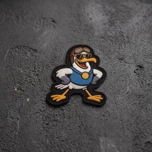 May include: An embroidered patch featuring a cartoon seagull wearing a brown aviator cap and black sunglasses. The seagull has white feathers, a blue vest with a gold circular emblem, and yellow feet. The design is outlined in thick black thread.