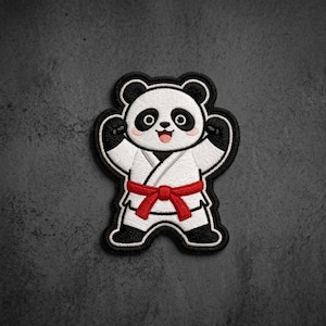 May include: An embroidered patch featuring a white and black panda bear wearing a white martial arts uniform with a red belt. The panda has its arms raised, a smiling expression with a pink tongue, and pink cheeks, outlined in black thread.