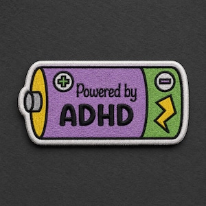 May include: A rectangular embroidered patch shaped like a battery with a white border. The center is purple with the black text Powered by ADHD. The left side is yellow with a green plus sign, and the right side is green with a yellow lightning bolt.