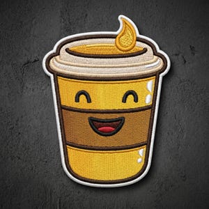 May include: An embroidered patch shaped like a yellow coffee cup with a smiling face. The cup features a brown sleeve, a white lid, and a small yellow flame icon on top. The design uses yellow, brown, white, and red thread with a white border.