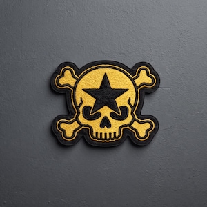May include: An embroidered patch featuring a yellow skull with a black star on its forehead, positioned in front of two crossed yellow bones. The design is outlined in black thread, creating a high-contrast graphic emblem with a textured surface.