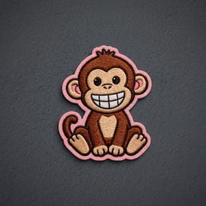 May include: An embroidered patch featuring a cartoon monkey with brown fur, a tan face, and a wide, toothy grin. The monkey is sitting down with its tail curled to the side. The entire design is outlined with a thick, light pink border.