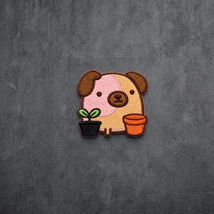 May include: An embroidered patch featuring a tan and pink cartoon dog with brown ears. The dog is positioned between a small black pot containing a green sprout and an empty orange terracotta-style pot, all outlined in dark brown thread.