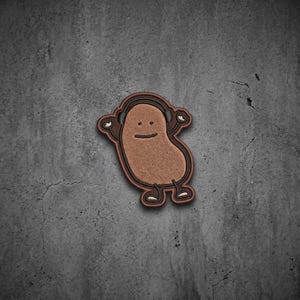 May include: An embroidered patch featuring a brown, bean-shaped character with a simple line-drawn face, wearing black headphones. The character has two arms raised and two legs, all outlined in dark brown thread against a textured background.