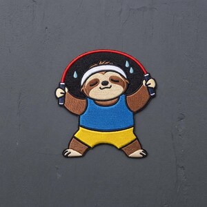 May include: An embroidered patch featuring a brown sloth wearing a white headband, a blue tank top, and yellow shorts. The sloth is holding a red jump rope over its head, with small light blue sweat droplets depicted around the rope.