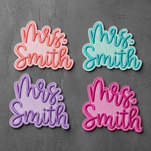 May include: Four embroidered fabric patches featuring the text Mrs. Smith in a cursive script font. The patches are colored in shades of coral, teal, purple, and bright pink, each with a matching border that follows the shape of the lettering.