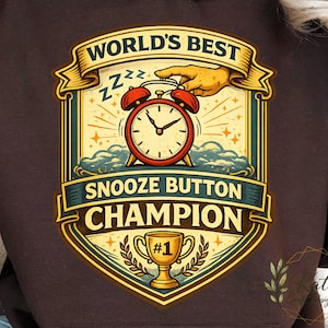 May include: Brown hoodie with a graphic featuring a red alarm clock, the words "WORLD'S BEST" and "SNOOZE BUTTON CHAMPION". The design includes a gold trophy and a hand reaching for the alarm clock.