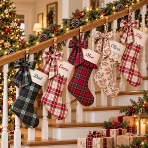 Può includere: Cinque calze di Natale appese alla ringhiera di una scala in legno. Ogni calza presenta un risvolto in tessuto con un nome ricamato in corsivo rosso o nero: Dad, Emma, Mom, Oliver e Lily. Le calze hanno motivi scozzesi o floreali.