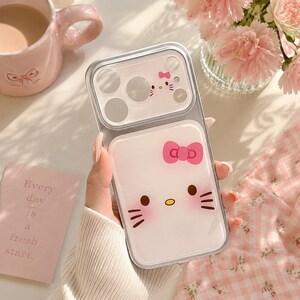 A hand holding a Hello Kitty phone case with a bow, surrounded by a pink mug, a vase of pink flowers, and a pink card with the phrase "Every day is a fresh start."