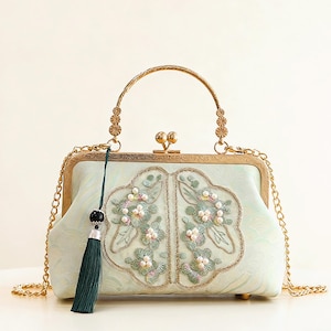 以下が含まれることがあります： ゴールドのハンドルとチェーンストラップが付いた、水色のハンドバッグ。 バッグには、パールアクセントと濃い緑色のタッセルが付いた花の刺繍が施されています。 クラスプと足は金色の色合いです。