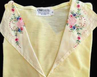 May include: A pale yellow vintage top with a V-neck and a decorative collar. The collar is off-white and features embroidered pink, blue, and green floral designs. The tag reads "Ohrbach's Made in Hong Kong".