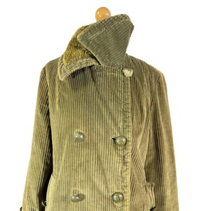 May include: Olive green corduroy coat with a double-breasted design. The coat features a wide collar with a faux fur lining and large, round buttons. The coat is displayed on a wooden hanger.