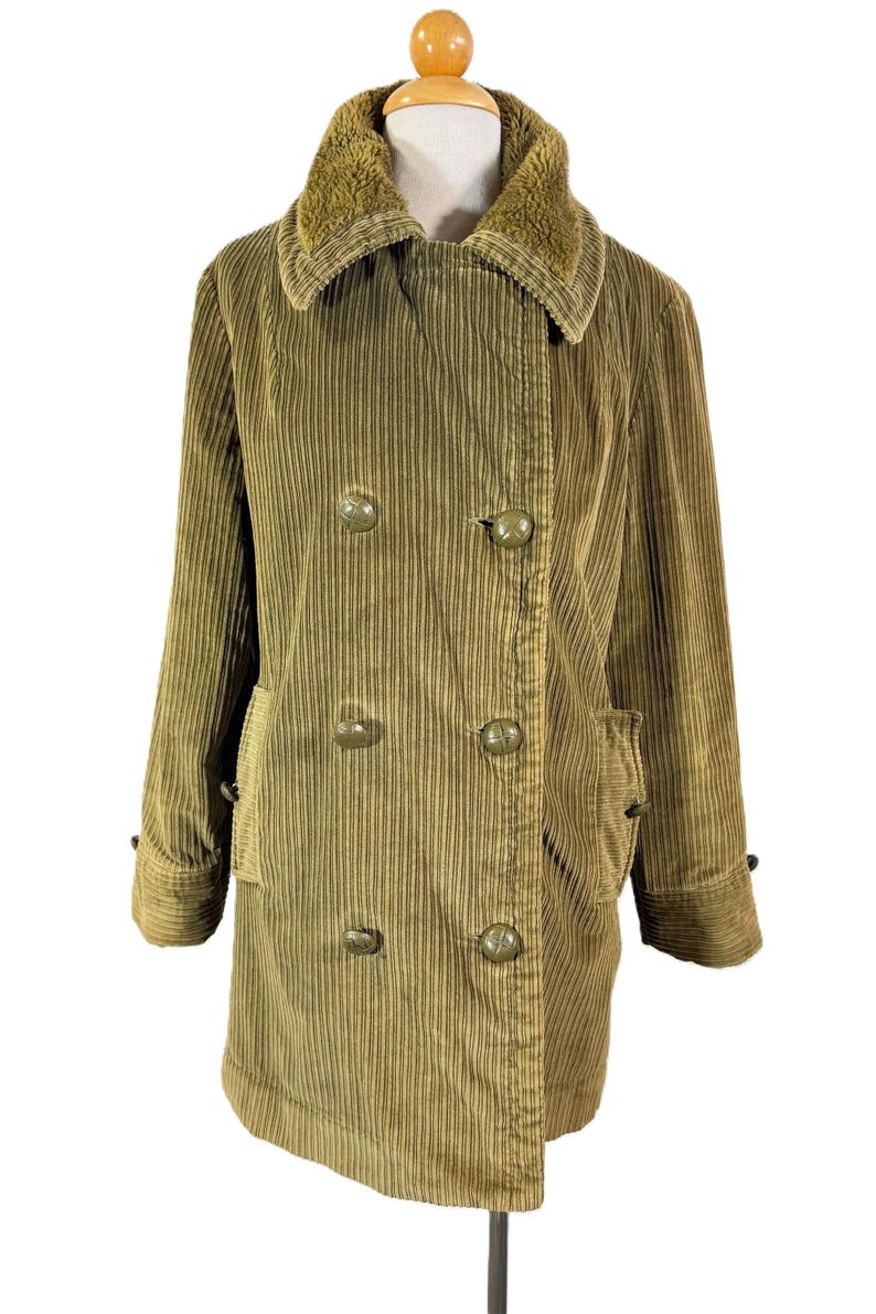 May include: A vintage olive green corduroy coat with a faux fur collar. The double-breasted coat features large, round buttons and two front pockets. The coat is displayed on a mannequin.