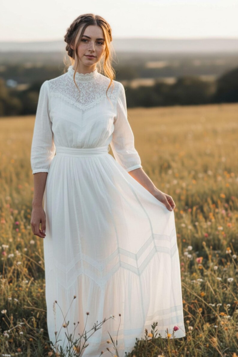 May include: A white dress with a high neckline and lace detailing. The dress has three-quarter sleeves and a flowing skirt. The person is standing in a field of wildflowers. The dress appears to be made of a lightweight fabric.