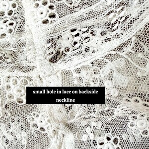 May include: Close-up of white lace fabric with a delicate floral pattern. The lace features a small hole on the backside neckline, as indicated by the text in the image. The intricate design is visible throughout the fabric.