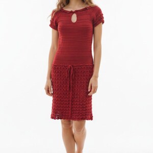 May include: A red knitted dress with short sleeves and a keyhole neckline. The dress features a textured skirt with a drawstring waist. The model is standing barefoot against a white background. The dress is knee-length.